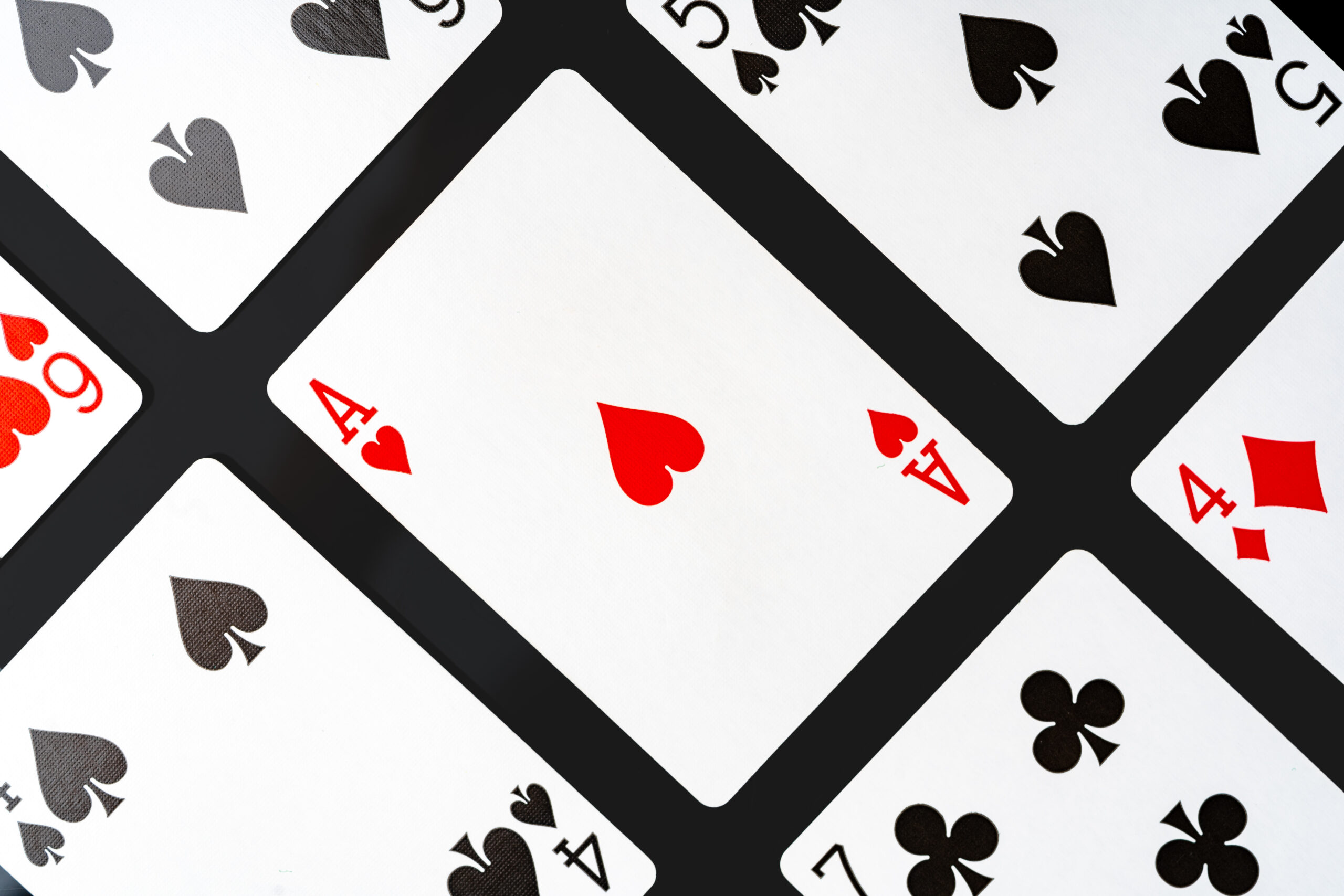 Close-up of playing cards arranged at an angle on a solid black background. In the center of the frame is the Ace of Hearts, surrounded by partially visible cards, including the five of spades, seven of clubs, and four of diamonds.